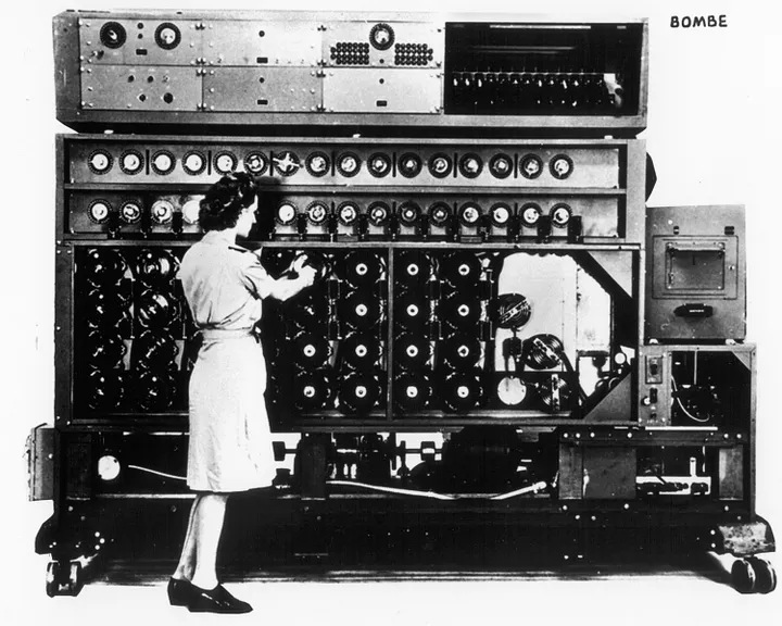 A wartime operator working at a Bombe codebreaking machine, its face covered in rotating drums